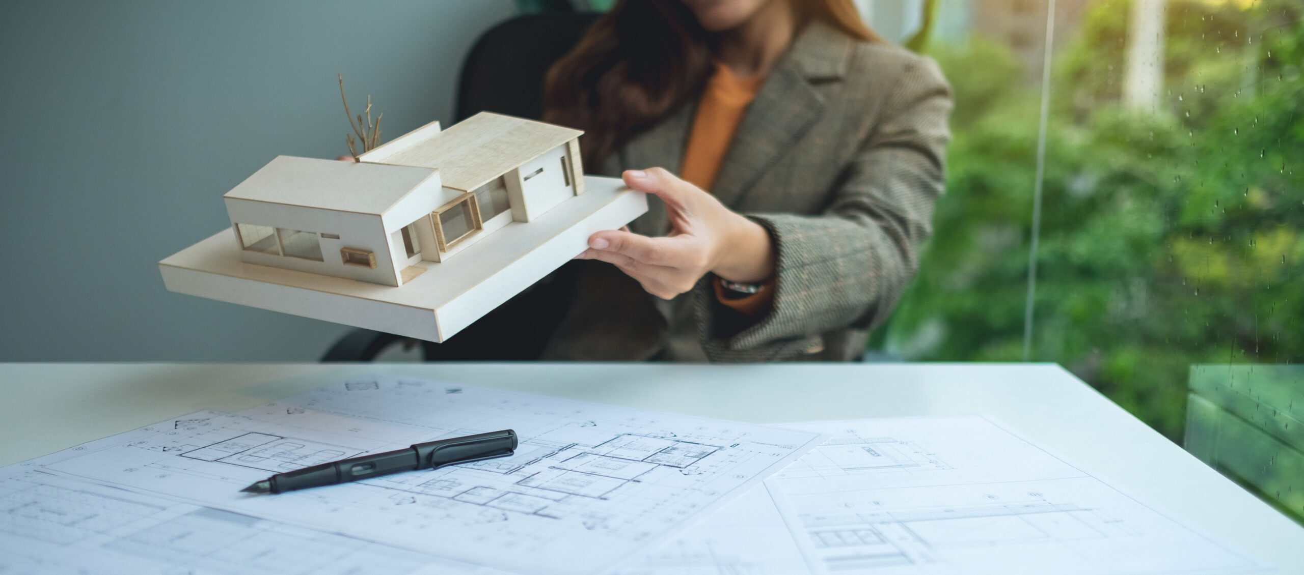 A female architect holding and working on an architecture house model with shop drawing paper in the office